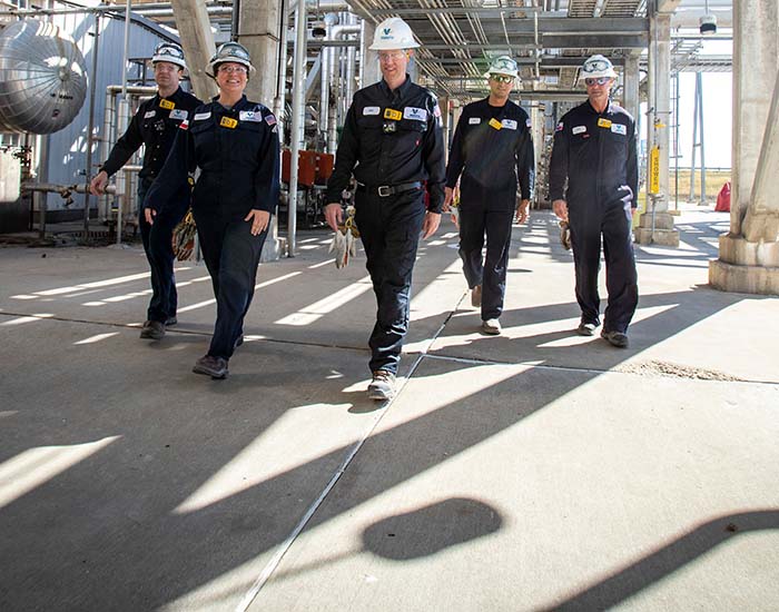Team of five Valero employees walking through the Three Rivers refinery, surrounded by equipment.