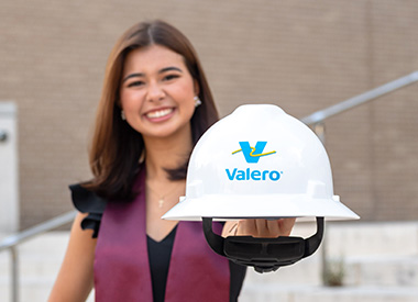 A college graduate holds a Valero hard hat.