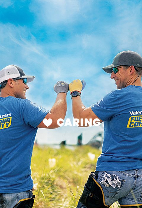 Two Valero employees at a volunteer give each other a friendly fist-bump. Text in the image reads "CARING."