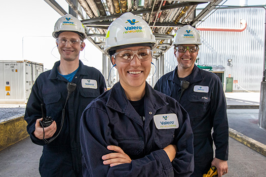 Three Valero Renewables employees stand together, smiling. The woman and two men are wearing standard PPE, including hard hats, protective glasses and NOMEX gear.