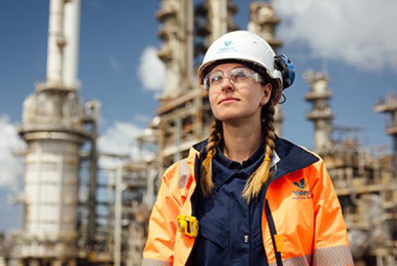 A woman engineer at Valero's Pembroke Refinery stands in front of refinery equipment and looks to the sky.