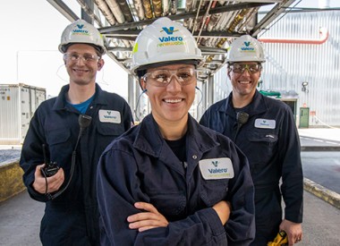 Three Valero Renewables employees stand together, smiling. The woman and two men are wearing standard PPE, including hard hats, protective glasses and NOMEX gear.