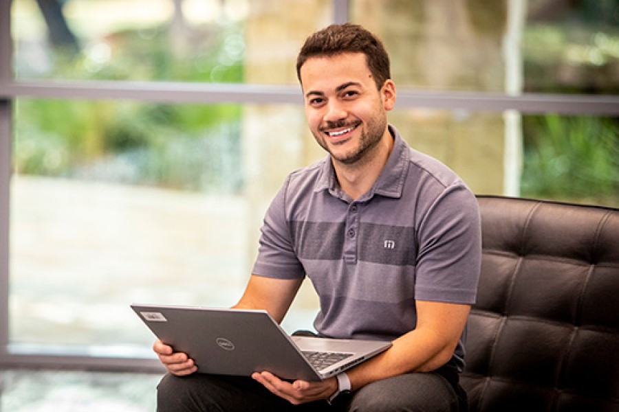 A Valero employee on a chair smiles and works on a laptop.