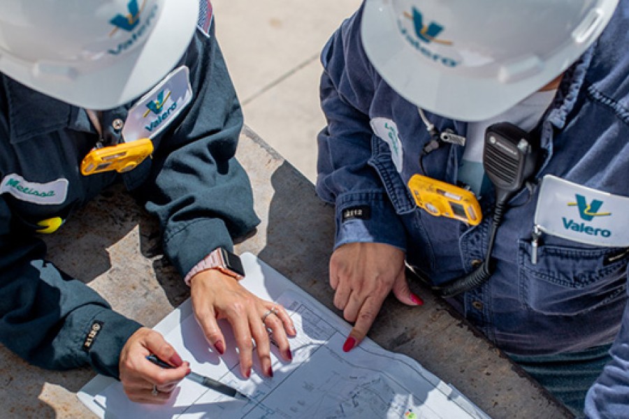 Two Valero employees in full PPE are at a refinery and reviewing schematics.