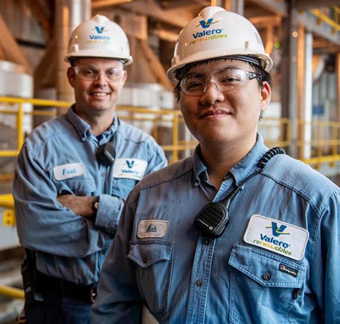 Two Valero employees stand together and smile in front of equipment.